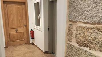 Un pasillo con una puerta de madera con la leyenda “4B”, un extintor y una pared de piedra.