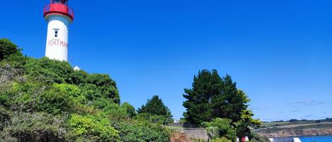 A lighthouse named "Port Man" with a red top, surrounded by greenery and a clear blue sky.