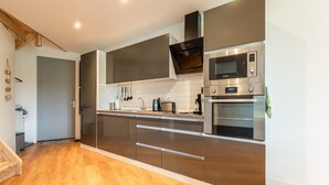 A modern kitchen with stainless steel appliances, wooden flooring, and a minimalist design.