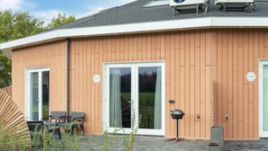 A modern building with wooden siding, large sliding glass doors, and a small outdoor seating area with chairs.