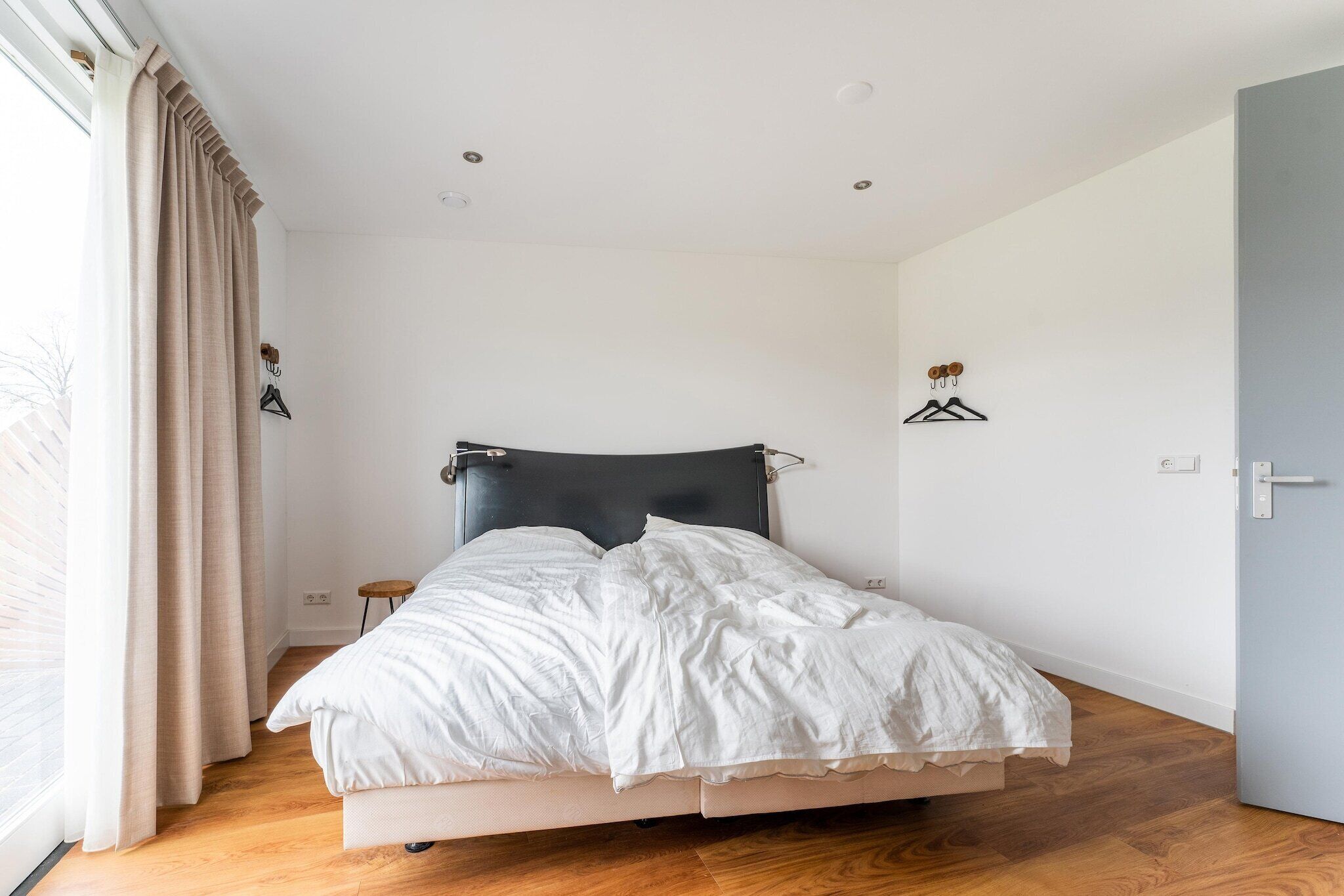 A bedroom with a bed, wooden floor, white walls, and a door.