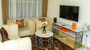 A living room with a sofa, a round coffee table, a flat-screen TV, and a small side table. - Lux suites Jimka Apartments Kisumu (Kisumu)