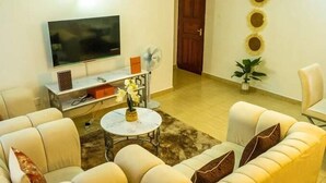 A living room with a flat-screen TV, a coffee table with a vase, and a sofa with cushions. - Lux suites Jimka Apartments Kisumu (Kisumu)