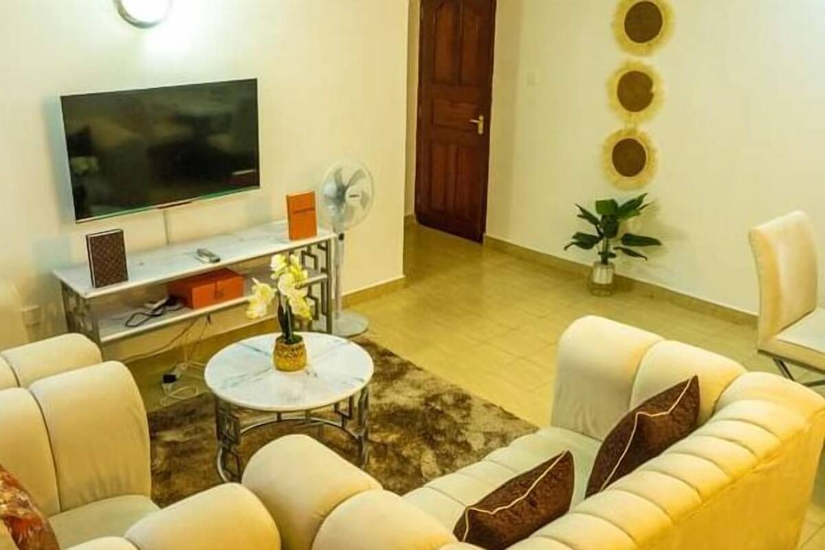 Una sala de estar con televisor de pantalla plana, una mesa de centro con un florero y un sofá con cojines.