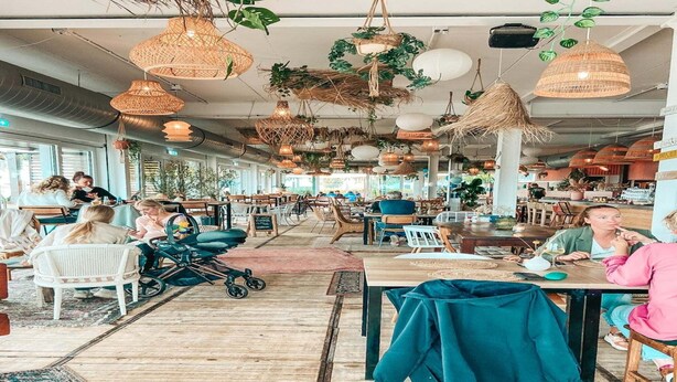 Un restaurant espaiós amb alts sostres, làmpades de vimet penjants i diferents disposicions d'aules, com taules i caires.