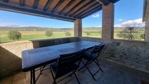 An outdoor patio with a stone table and chairs, a wooden ceiling, and a view of a green landscape.