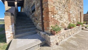 A stone building with a staircase leading to a door, surrounded by potted plants.