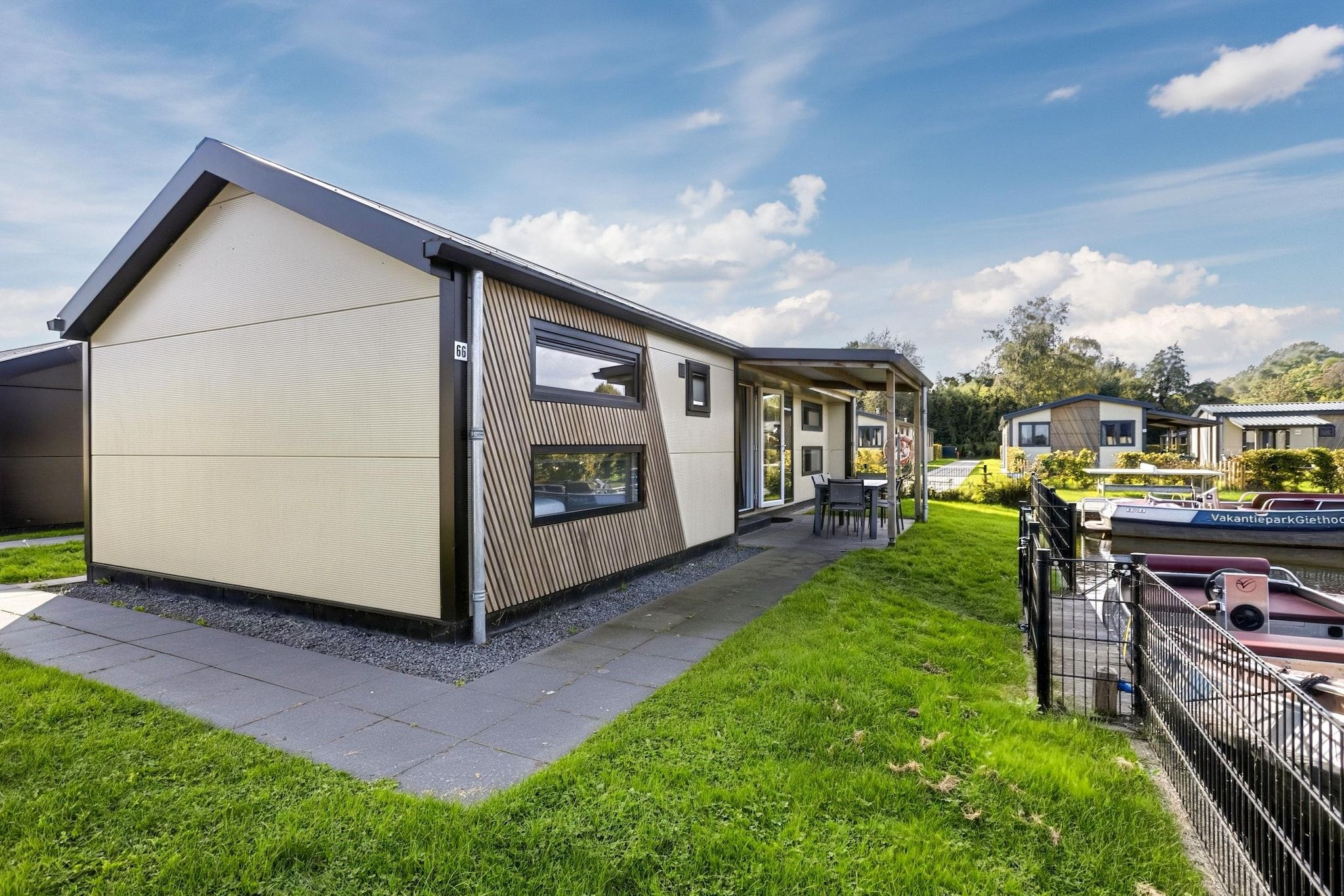 Ein modernes Ferienhaus mit überdachter Terrasse, Bootssteg und gepflegtem Rasen.