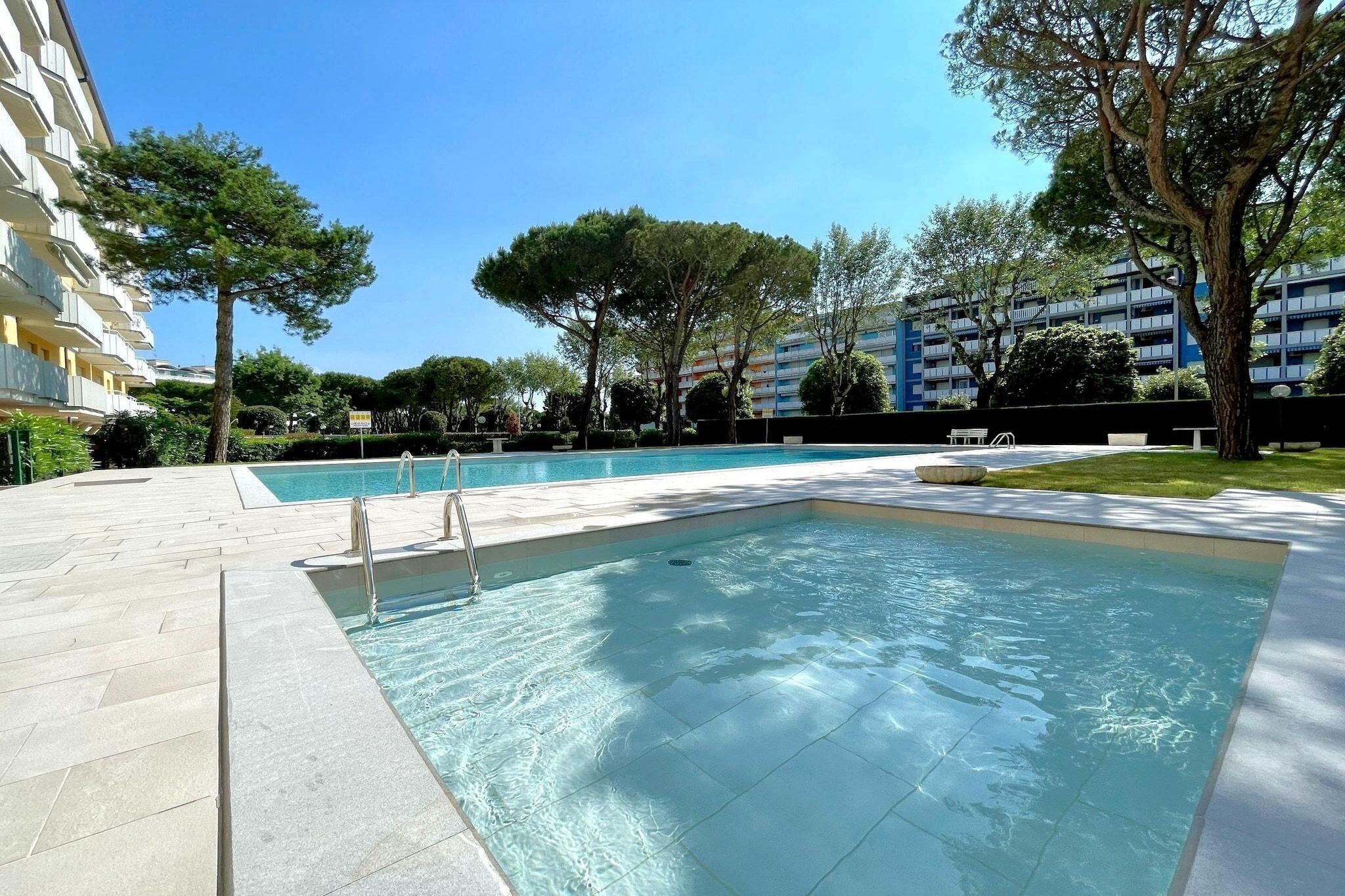 A swimming pool with a tiled deck, surrounded by trees and buildings.