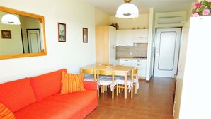 Ein gemütlicher Wohnraum mit einem roten Sofa, einem Esstisch mit Stühlen, einer Küchenzeile und einer Tür.