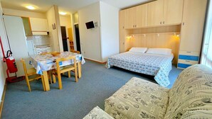 A compact room with a bed, a sofa, a table with chairs, a kitchenette, and a TV. - Holiday Home in Caorle near Spiaggia Tartaruga (Porto Santa Margherita (VE))
