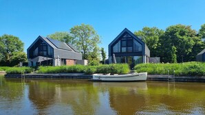 A modern building with a sloped roof and large windows, situated next to a calm water body. - Water Villa in Balk with Private Jetty (Balk)