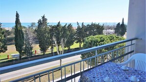 A balcony with a table set for dining, overlooking a road and greenery with a clear view of the sea. - Caorle Holiday Home with Terrace (Caorle (VE))
