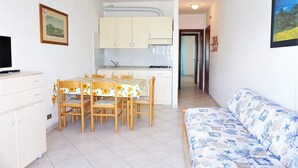 A compact kitchen with white cabinets, a dining table with chairs, a sofa, and a TV on a cabinet. - Caorle Holiday Home with Terrace (Caorle (VE))