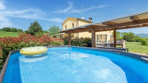 A swimming pool with a yellow inflatable ring, surrounded by a wooden pergola and a house in the background. - Country escape in Matelica (Matelica)