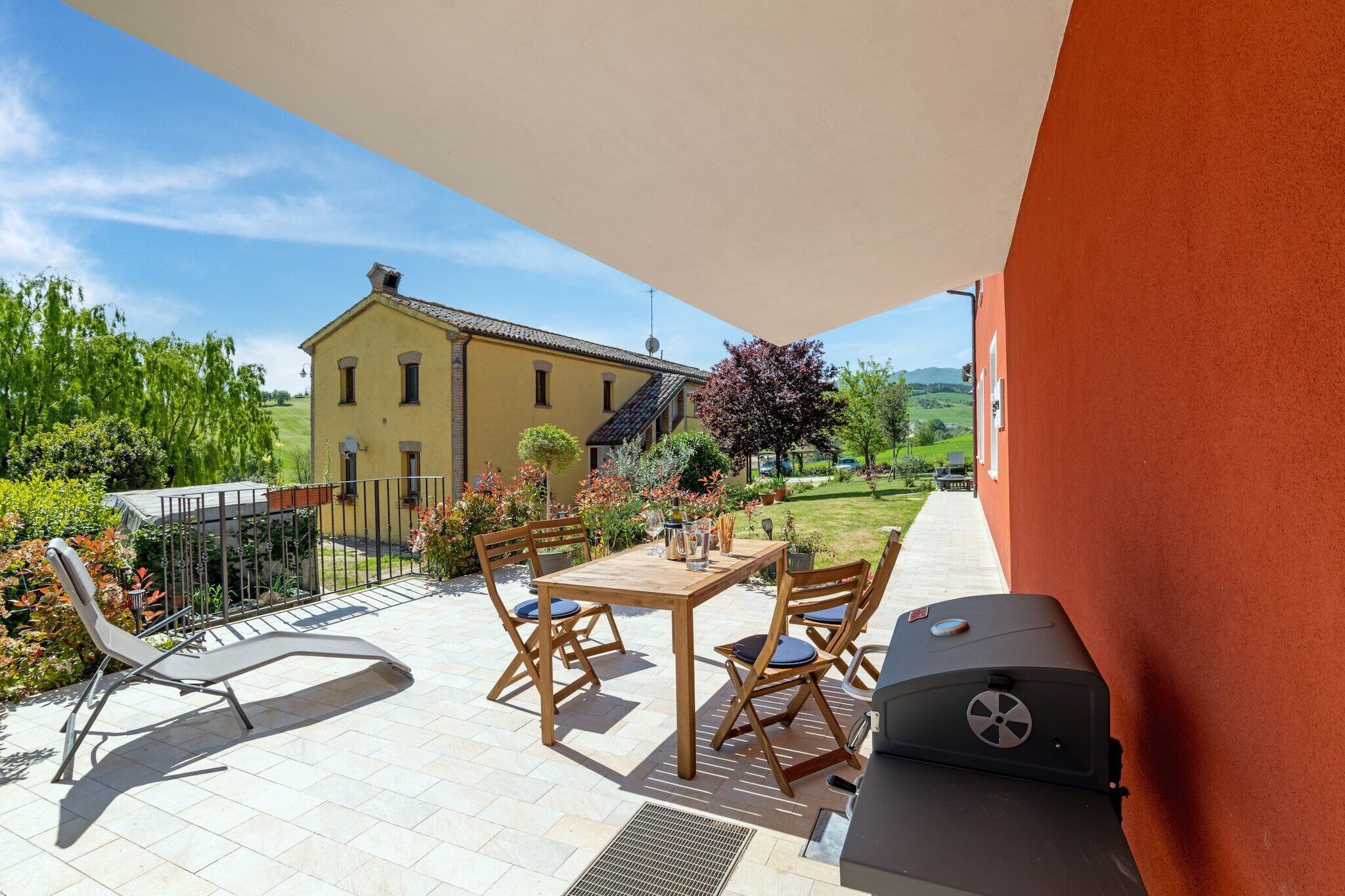 A patio with a table and chairs, a grill, and a view of a house in the background.