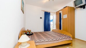 A bedroom with a bed, a nightstand, a lamp, a wardrobe, and a television.