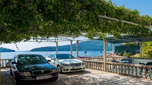 Two cars parked under a covered area with a view of the sea and hills.