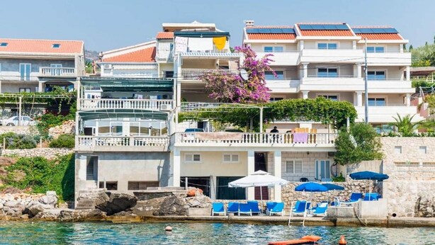 A coastal hotel with multiple balconies, a pool area with sun loungers, and a view of the sea.