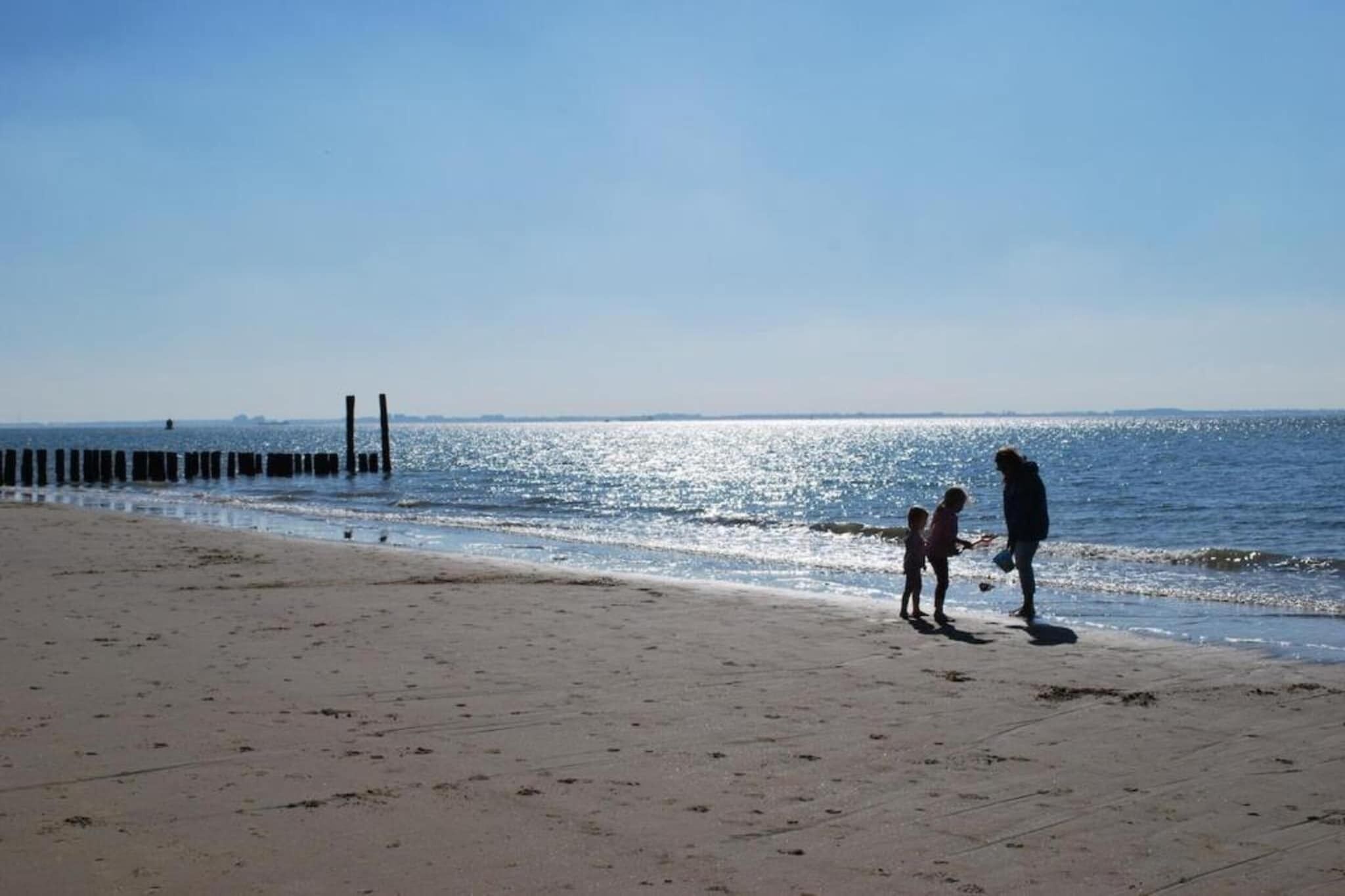 Una spiaggia con cielo sereno, una persona e un bambino vicino alla riva, e un molo sullo sfondo.