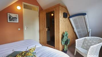 A bedroom with a bed, a wooden door, a chair, and a potted plant.