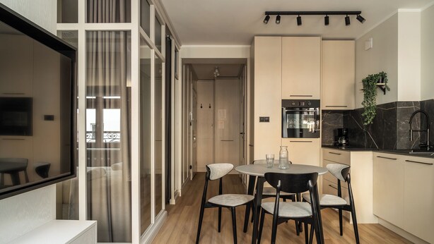 A modern kitchen with a dining area, wooden flooring, and a sliding glass door leading to a balcony. - RentPlanet - Apartament Szczytnicka (Wroclaw)