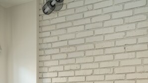 A neatly made bed with a beige blanket and pillows, a bedside lamp, and a white brick wall. - RentPlanet - Apartament Szczytnicka (Wroclaw)