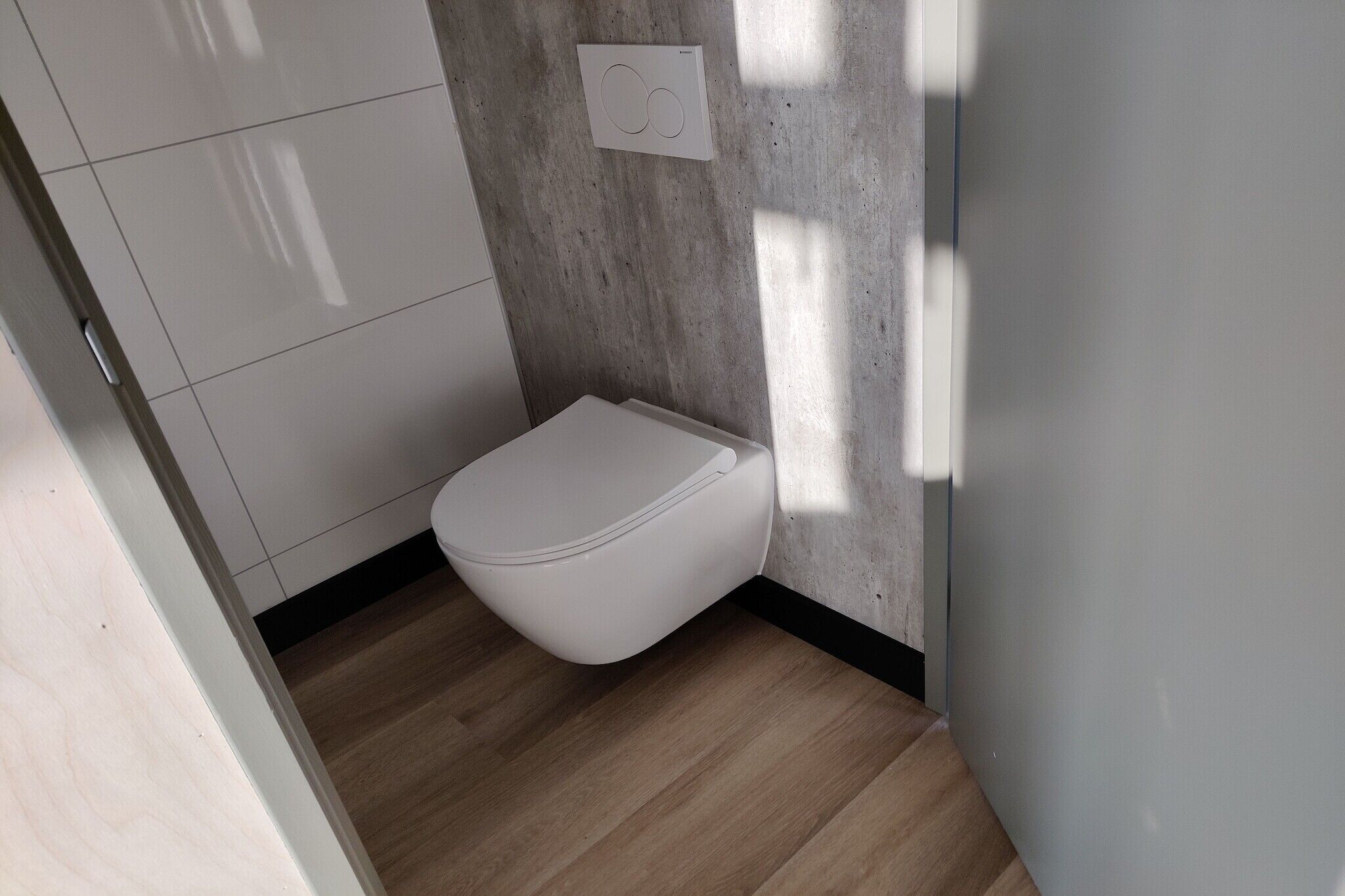 Een moderne badkamer met een toilet, een betonnen muur en een houten vloer.