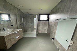 Une salle de bain moderne avec une douche à parois de verre, un grand miroir et un meuble-lavabo blanc.