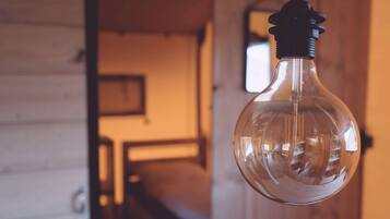 A clear glass light bulb hanging from a ceiling in a room with wooden walls and a visible staircase in the background.