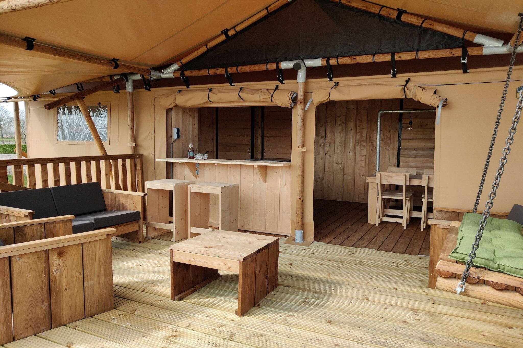En träveranda med en soffa, ett litet bord och en gunga.
