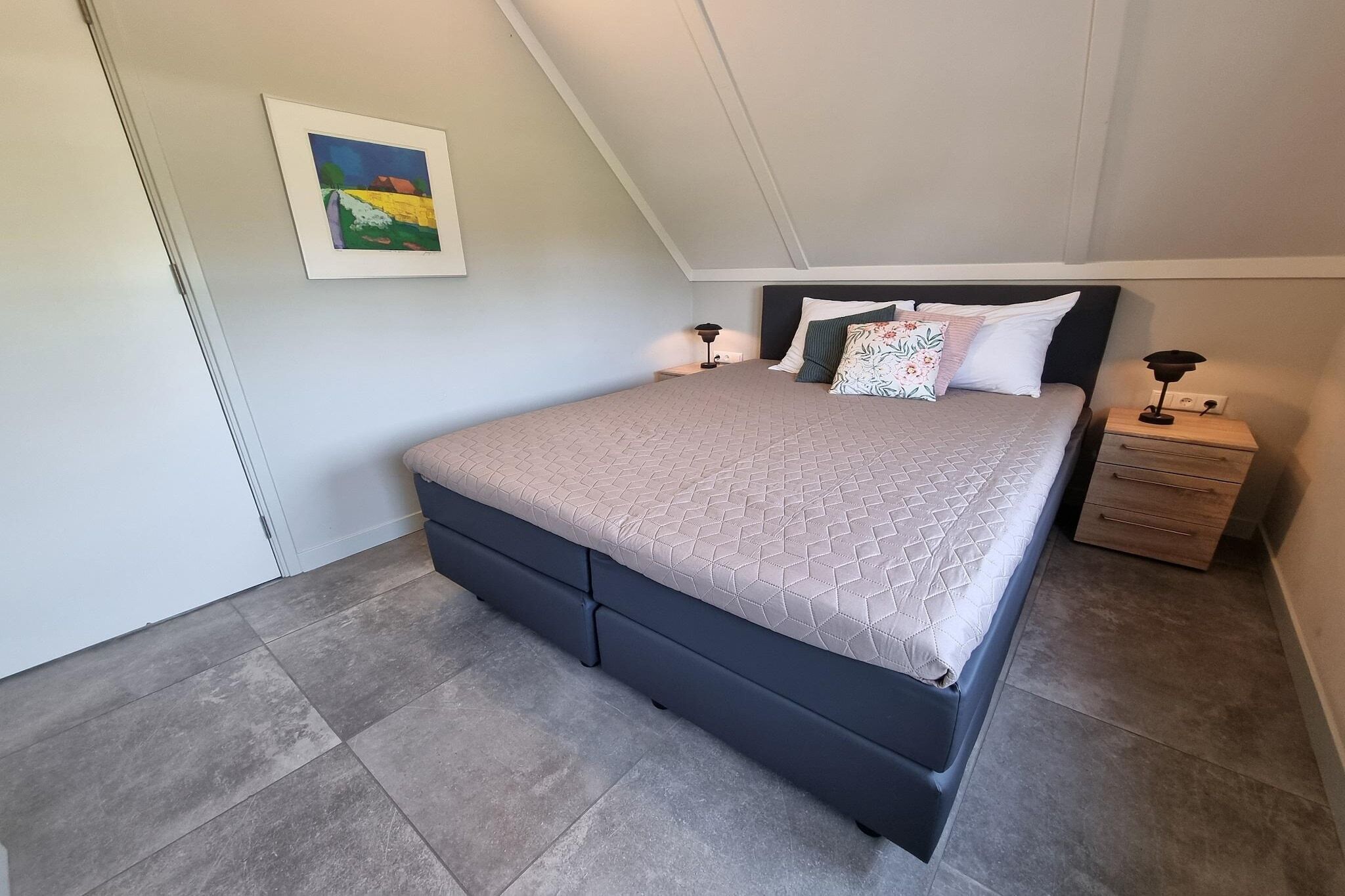 Ein Schlafzimmer mit Bett, Nachttischen, einem Wandbild und einer geneigten Decke.