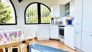 Een keuken met witte kastjes, een fornuis en een eethoek met een tafel en stoelen.