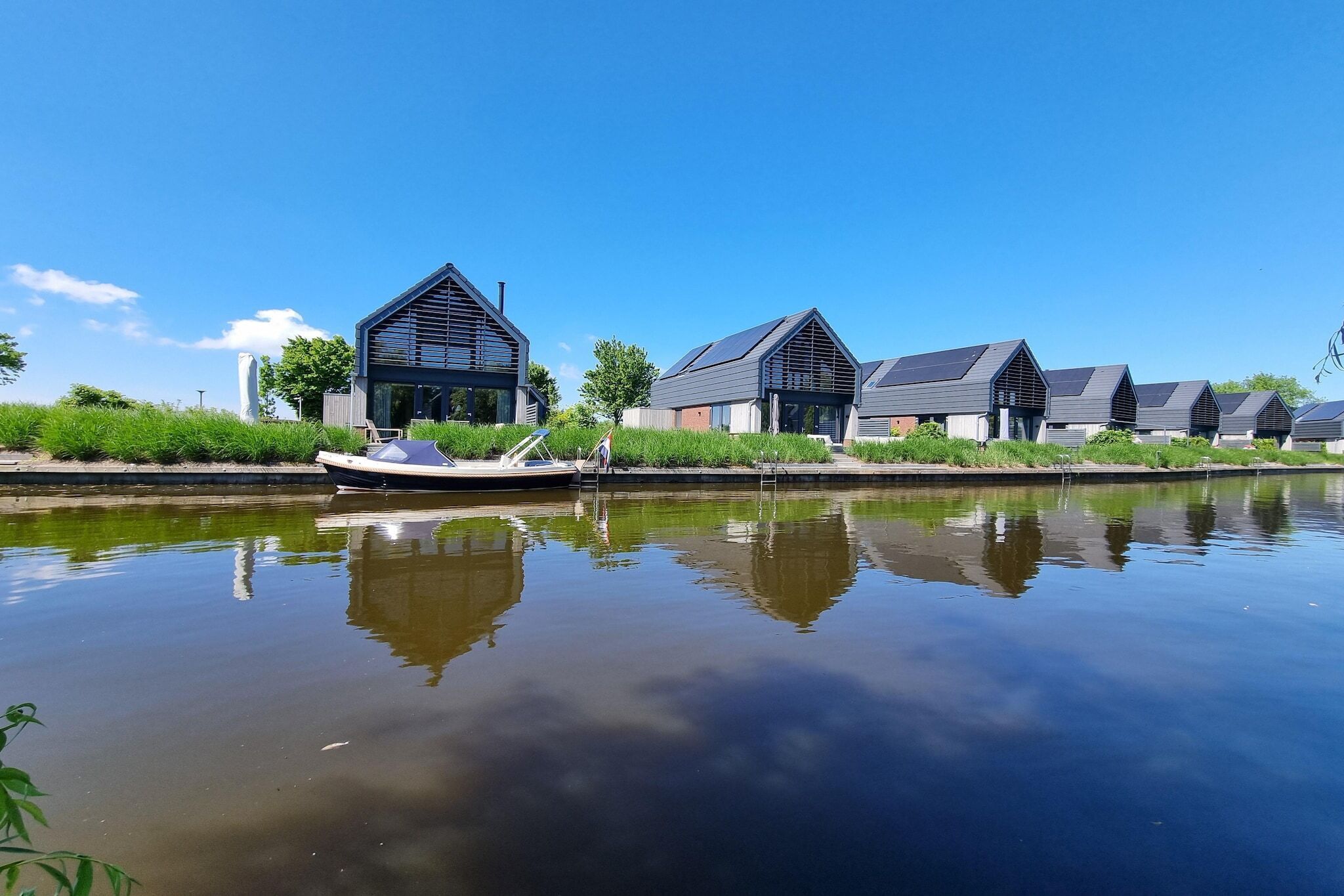 A row of modern houses by a calm river, with a boat docked in the foreground.