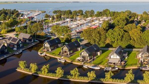 En småbåtshamn med förtöjda båtar, omgiven av hus med stora fönster och en gräsyta.
