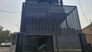 Un edificio de varios pisos con un diseño moderno, que cuenta con un balcón grande en el segundo piso y una entrada protegida por una reja.