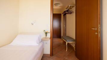 A bedroom with a bed, a bedside table with a lamp, a bench, and a door leading to a hallway with a coat rack.