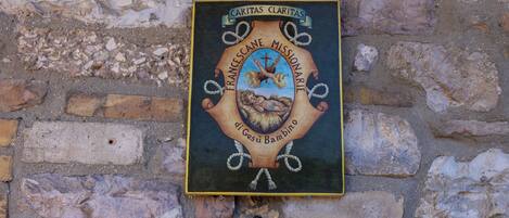 Una placa con la inscripción "CARITAS CLARITAS" y "MISIONERO FRANCISCANO" en una pared de ladrillo.