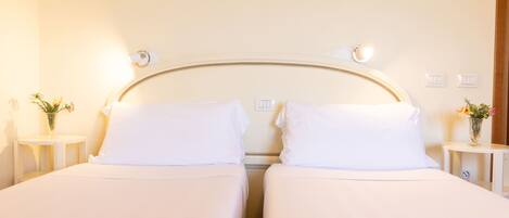 A hotel room with two single beds, bedside tables with lamps, and a wall-mounted light fixture.