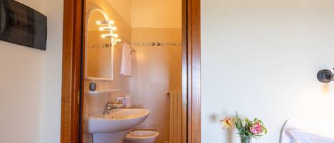 A bathroom with a sink, toilet, and shower area, and a table with a vase of flowers.