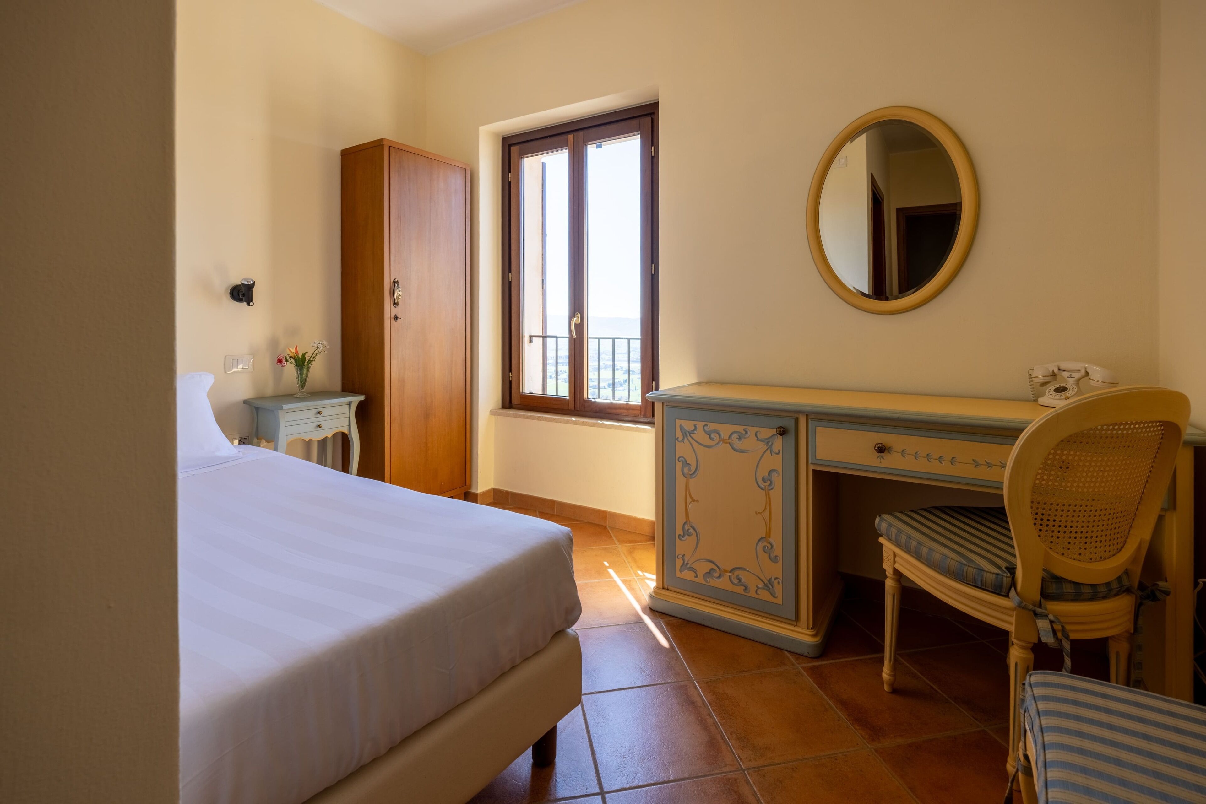 A bedroom with a bed, a dresser, a chair, a mirror, and a window with a view.