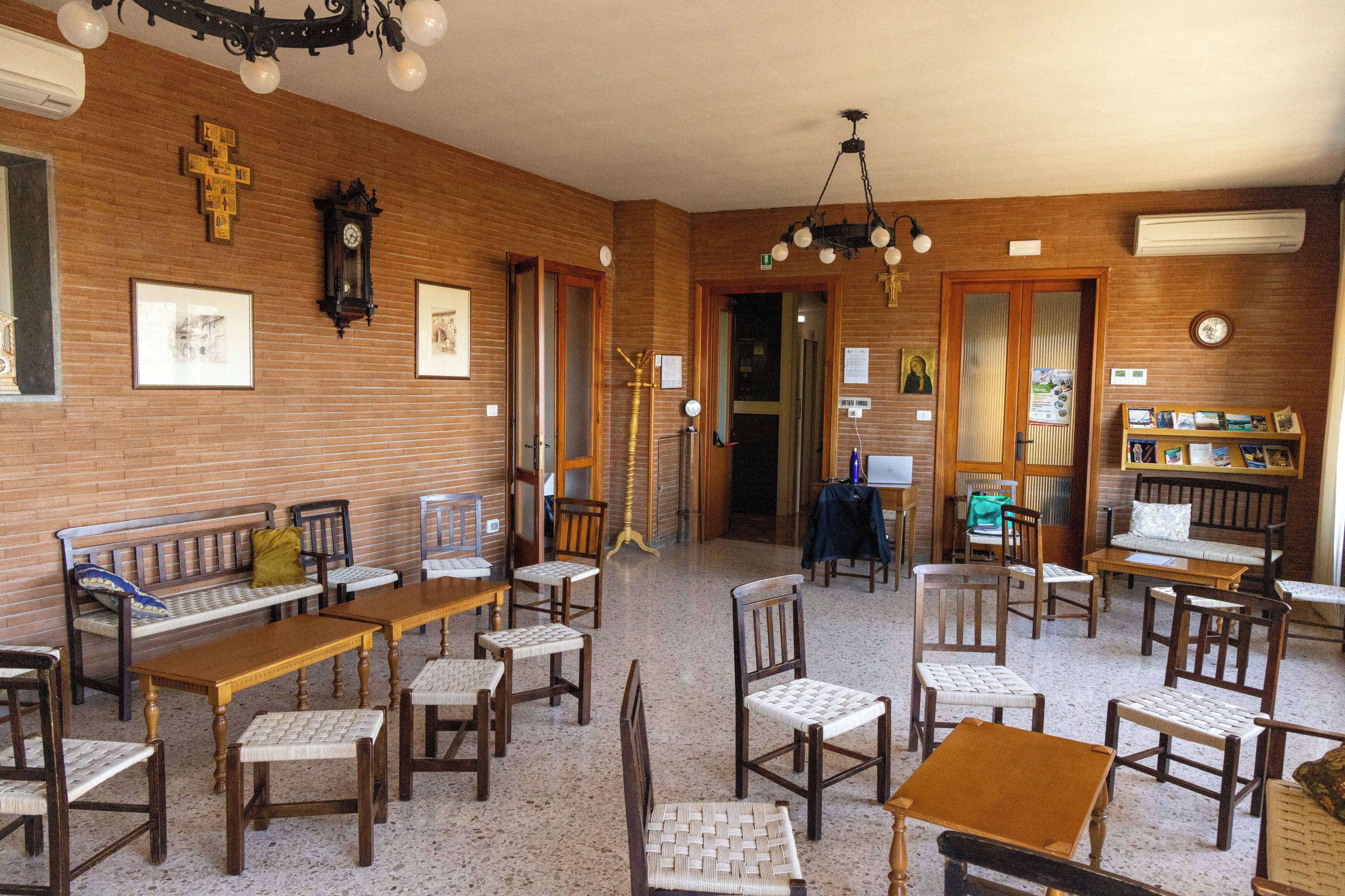 Une pièce aux murs en bois, avec un banc en bois, plusieurs tables et chaises, un lustre et une horloge.