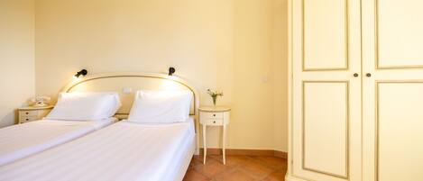Habitació d'hotel amb dos llits, una taula de nit amb una làmpada, una taula petita amb un ram i un armari.
