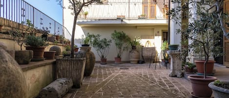 A courtyard with potted plants, stone walls, and a brick floor.