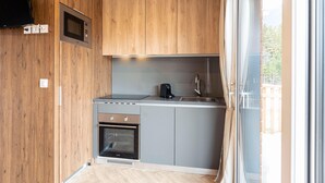 A compact kitchen with wooden cabinets, a built-in microwave, a stove, and a sink. - Beautiful tree house in the Gailtal valley (Kötschach-Mauthen)