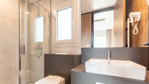 A modern bathroom with a glass-enclosed shower, a white toilet, a large mirror, and a white sink. - Beautiful tree house in the Gailtal valley (Kötschach-Mauthen)