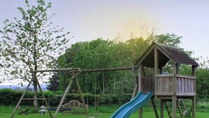 A wooden play structure with a slide and swings in a grassy area.