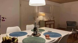 A dining area with a table set for two, a bottle of wine, and a fruit bowl.