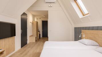 Quarto moderno com cama grande, televisão, cabeceira de madeira e claraboia.