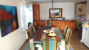 Un comedor con una mesa de madera, sillas coloridas y un cuadro grande en la pared.